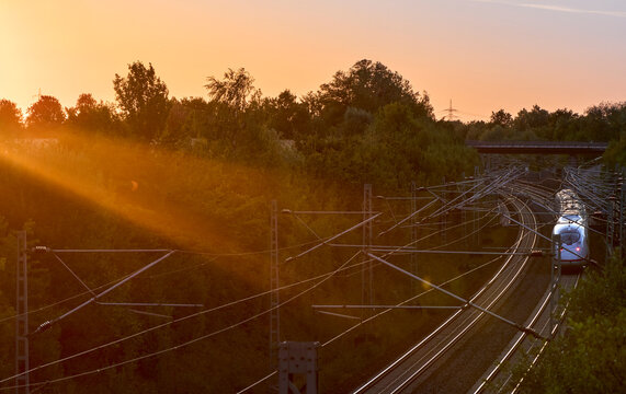 Intercity train traveling through a scenic railway corridor at sunset, surrounded by trees and overhead power lines. Stuttgart to Mannheim, Baden-W&uuml;rttemberg, Germany