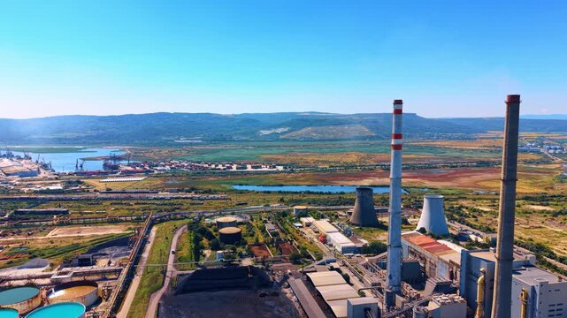 Power plant near the river and land area. A view of a power plant with tall chimneys next to a river and open land. The scene shows industry and nature together.