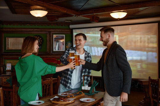 Friends cheer with beer glasses in cozy pub interior