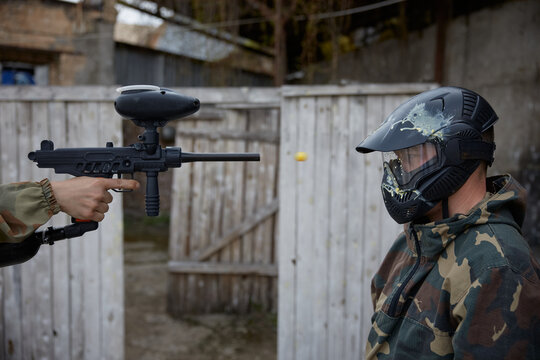 An individual is pointing a military weapon at a soldier wearing a helmet on a field