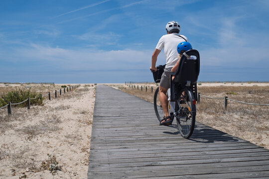 Man and Little Girl in Helmets Cycling Together on an E-Bike Near the Ocean
