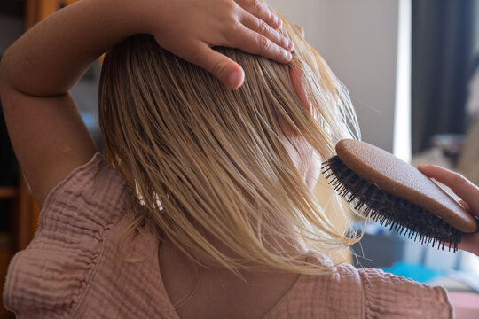  girl in a pink dress brushing her damp hair on a brown couch.