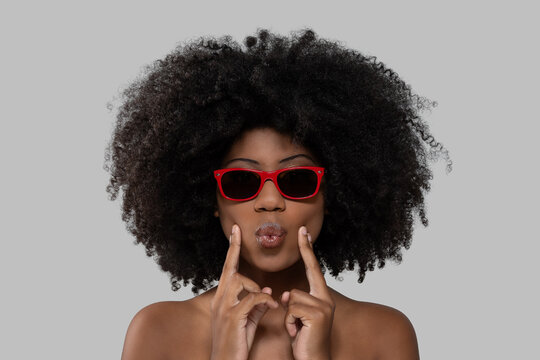 Portrait of young Black woman with afro puckering lips wearing red sunglasses