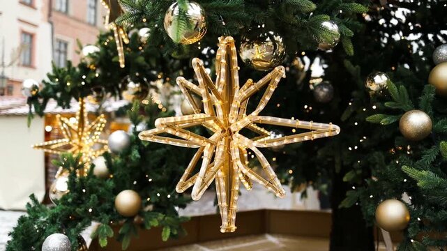 Close up of an outdoor Christmas tree adorned with shiny gold and silver baubles and glowing lights on a historic European city square.