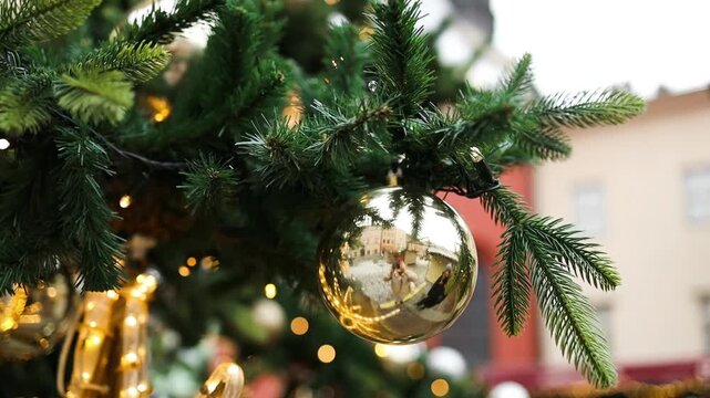 Close up of an outdoor Christmas tree adorned with shiny gold and silver baubles and glowing lights on a historic European city square.