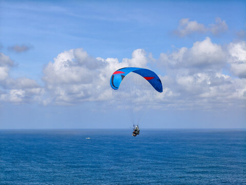 Paraglider Flying High Over Blue Ocean Water Against Cloudy Sky
