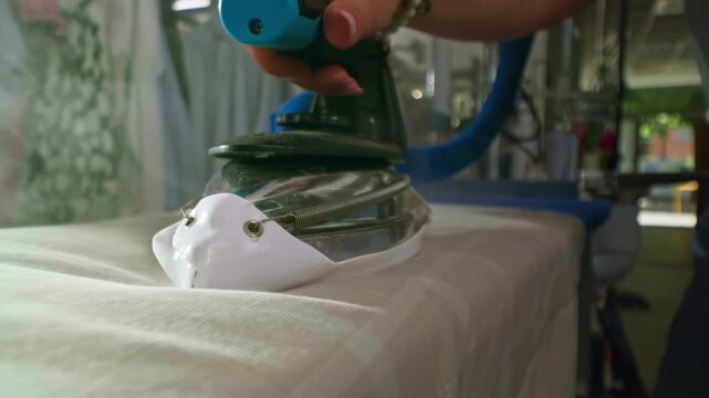 Cinematic close-up of a hot iron gliding smoothly over fabric on an ironing board, captured in slow motion, soft steam, dramatic lighting, realistic textile textures, elegant movement.