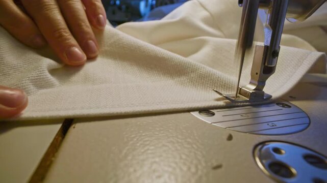 Cinematic macro shot of elderly hands guiding fabric through a sewing machine, needle moving in slow motion, soft dramatic light, detailed textures, authentic craftsmanship.