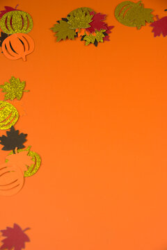 Glittering and paper autumn leaves and pumpkins decorating an orange background, providing copy space for seasonal designs