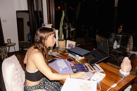 Woman using laptop at cluttered home desk during night work session