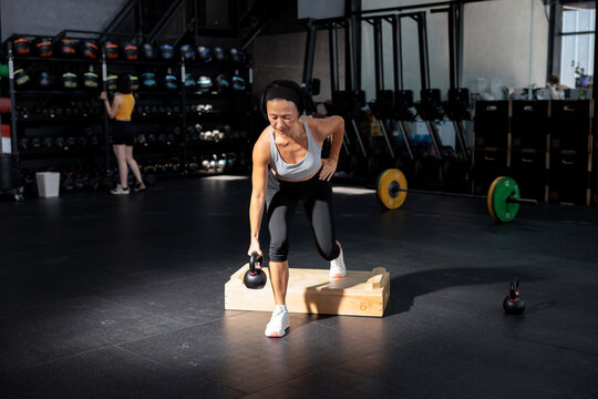 Woman performing kettlebell step-up exercise in gym