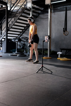 Woman filming kettlebell workout in gym.