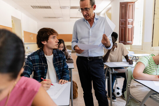 Teacher talking with student in school classroom during exam