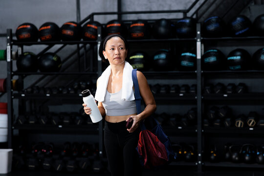 Woman at gym with towel, water bottle, and gym bag.