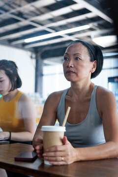 Woman with drink at table, another person in background.