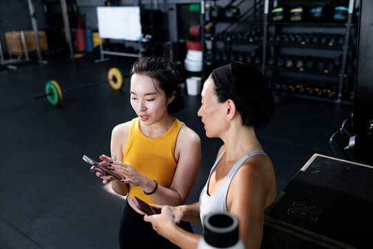 Two women look at a phone in a gym.
