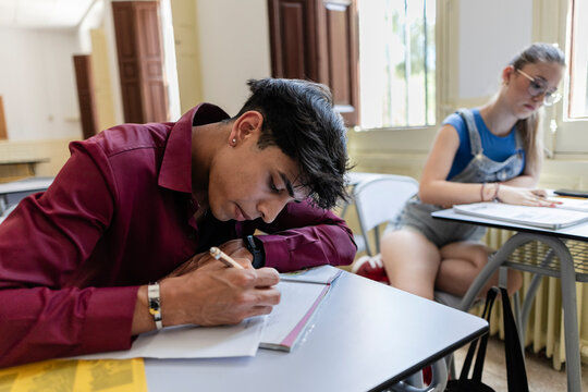 Male student studying for exam writing notes in classroom