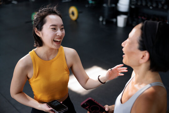 Two women laughing together at the gym, holding phones.