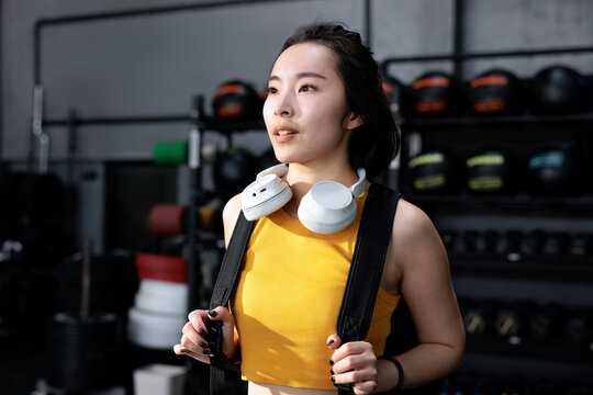 Woman with headphones and backpack in a gym.