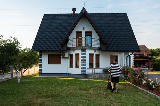 Man mowing front lawn outside detached family home at golden hour