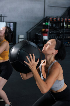 A focused woman performs wall ball exercises in a gym.