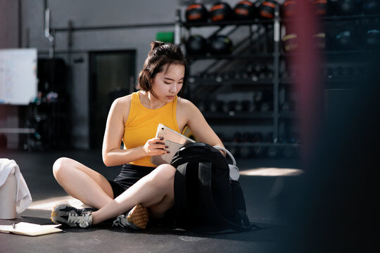 Woman with tablet and backpack in gym setting.