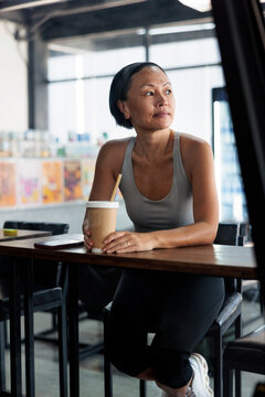 Woman with coffee cup looks thoughtfully out window.