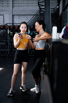 Two women looking at phones in a gym.
