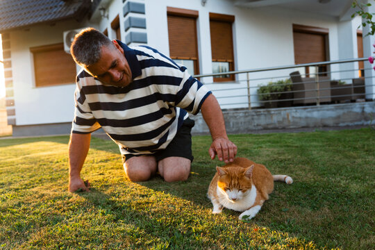 Man spending time with a ginger cat on a grassy lawn