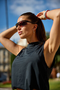 Woman adjusting her hair while wearing sunglasses and a dark top
