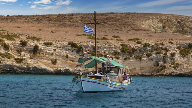 A boat with a Greek flag sails along rocky shores, the sea is blue and calm, White Cliffs, White Beach, Makri Aspronisi Island, Natura 2000 area, boat trip, Aspronisi, Lipsi, Dodecanese, Greek Islands, Greece
