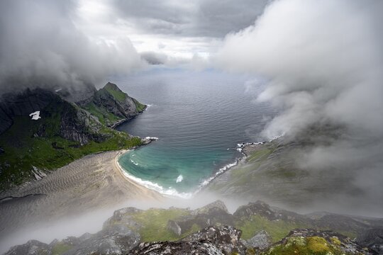 View from Helvetestinden summit, Bunesstranden sandy beach and blue sea, dramatic cloudy sky, Lofoten, Norway