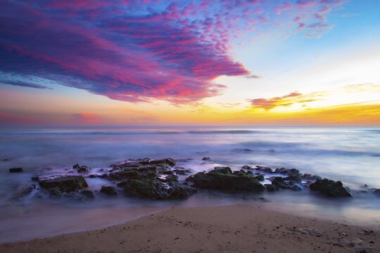 Vivid sunrise over calm coast with colorful sky and rocks in the foreground, sunset, Praia do Amado, Carrapateira, Algarve, west coast, Atlantic, Portugal