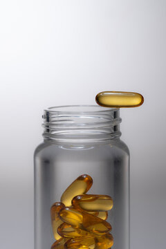 Glass bottle with golden omega-3 capsules, one balanced on the edge
