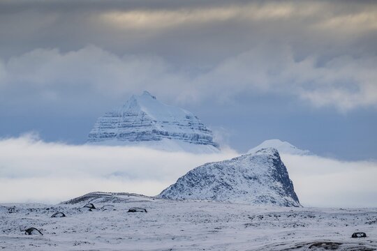Large rock behind clouds cover one of the three mountains Tee Kroner, Kongsfjord or Kongsfjorden, Spitsbergen archipelago, Svalbard, Norway