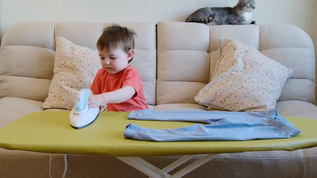 Baby is playing dangerously with a hot iron in the living room of the home, which could result in burns or harm to an unsupervised child. Kid aged about two years (one year ten months)