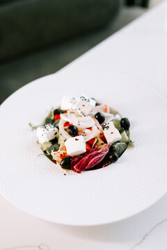 Fresh Greek salad served on a white plate with feta cheese and olives during a lunch time meal