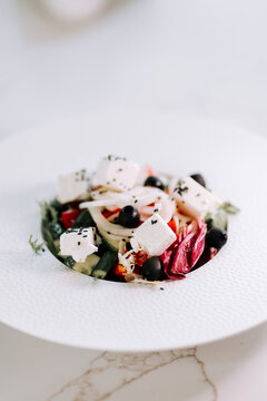 Greek salad with fresh feta cheese and black olives served on a clean white plate for a lunch meal