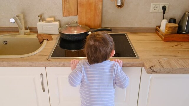 Child climbing up on kitchen counter with frying pan on stove. Dangerous situation at home. Toddler reaching for hot cooking equipment. Risk of burn or injury, safety home concept.