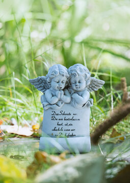 Kleine Zwillinge Engelsfiguren auf dem Friedhof im Gegenlicht im Gras