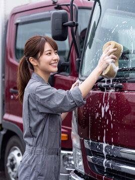 笑顔でトラックを洗車する作業着姿の若い女性ドライバー
