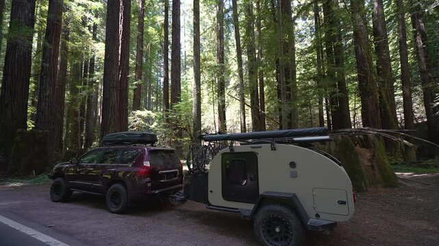 A woman prepares lunch in a teardrop camper trailer while parked near redwood trees in Navarro River Redwood State Park, California.