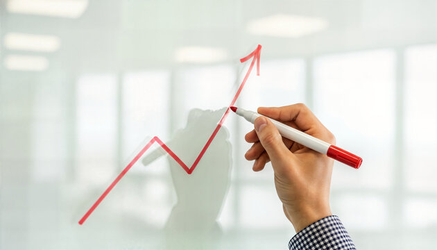 Hand drawing red arrow pointing upwards on transparent glass board illustrates financial growth and positive business performance trends in bright office setting.