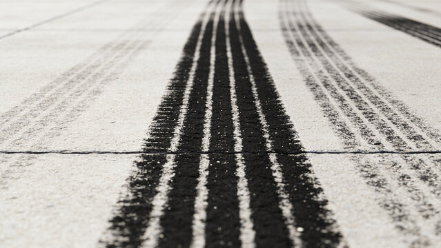 A stark and gritty close-up shot showcasing a series of dark, parallel tire tracks deeply imprinted on a light gray asphalt surface, evoking a sense of urban movement and industrial wear