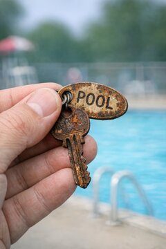 A person holds a key in front of a swimming pool, possibly indicating access or permission