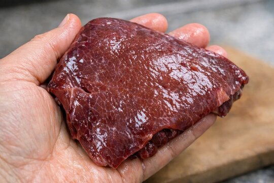 A person holds a piece of raw meat in their hand, possibly preparing for cooking or serving