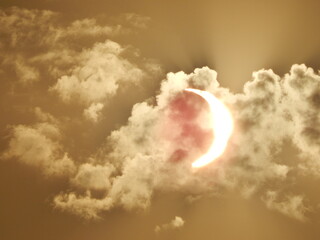 Éclipse solaire partielle du 12 août 2026 avec le Soleil en forme de croissant traversant les nuages, dans un ciel aux teintes dorées. © Manuela