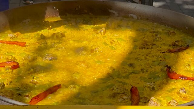 Close up shot of chef hand carefully placing roasted red pepper strips on top of simmering yellow saffron rice. Final stage of cooking traditional Spanish paella at an outdoor culinary event.