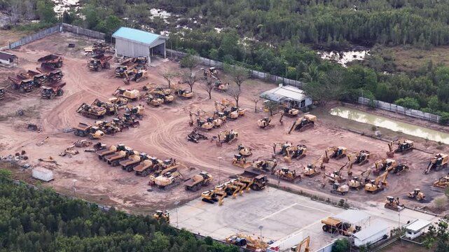 Rows of construction machines parked in a large dirt storage yard during the day