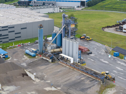 Skawina, Poland - 19 July 2026: Aerial view of the Colas asphalt plant with industrial silos, conveyor belts, and heavy machinery on a paved site near green fields and warehouses.
